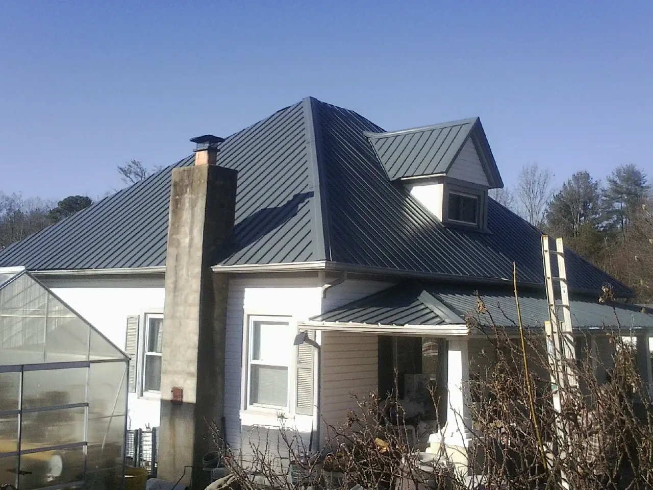 Dark blue standing seam metal roof on a white farmhouse with dormer — Slate & Tile Roof Repair by Roofing Brothers in Byron Center