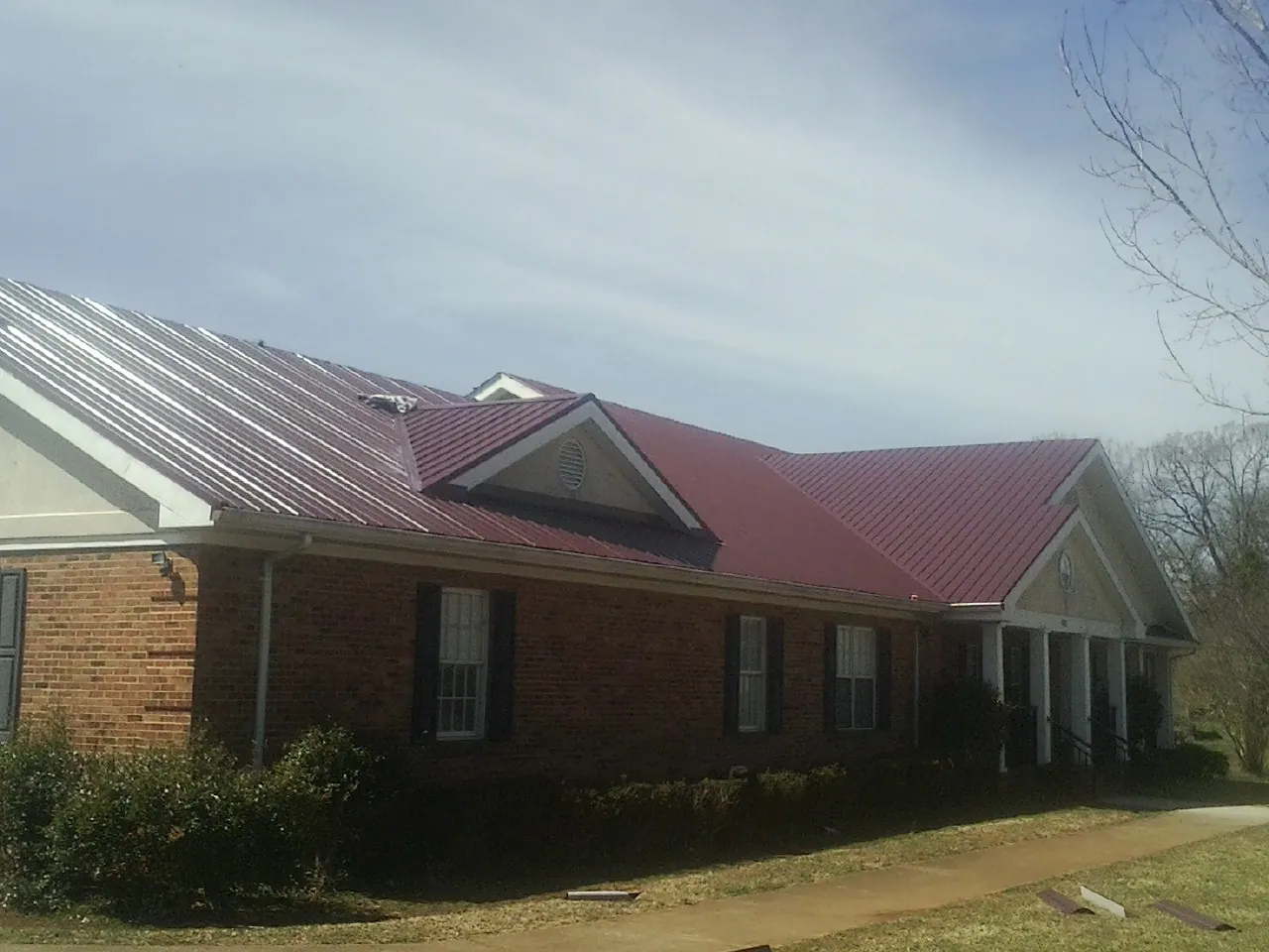Red metal roof with gabled entries on a long brick building, from a Hail Damage Roof Repair job in Byron Center