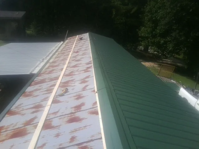 Old rusted panels beside newly installed green metal roofing — Wind Damage Roof Repair by Roofing Brothers in Byron Center