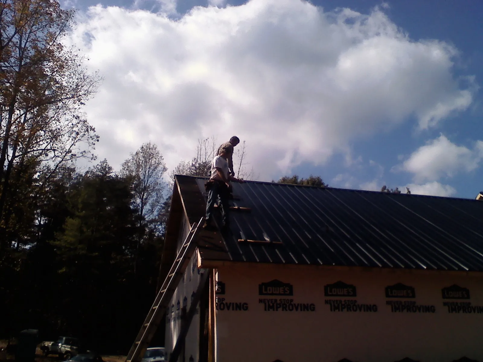 Roofer fastening dark metal panels high against a cloudy sky, from a Roof Inspection job in Byron Center