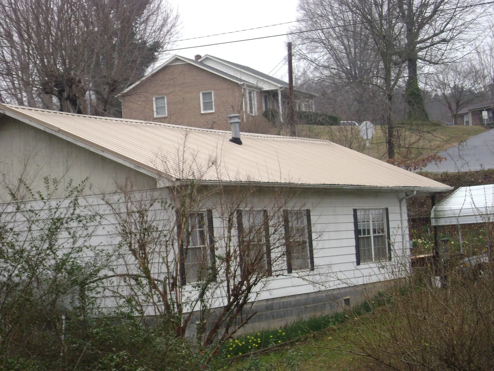 Tan metal roof on a white sided house set into a hillside — Commercial Roofing by Roofing Brothers in Byron Center