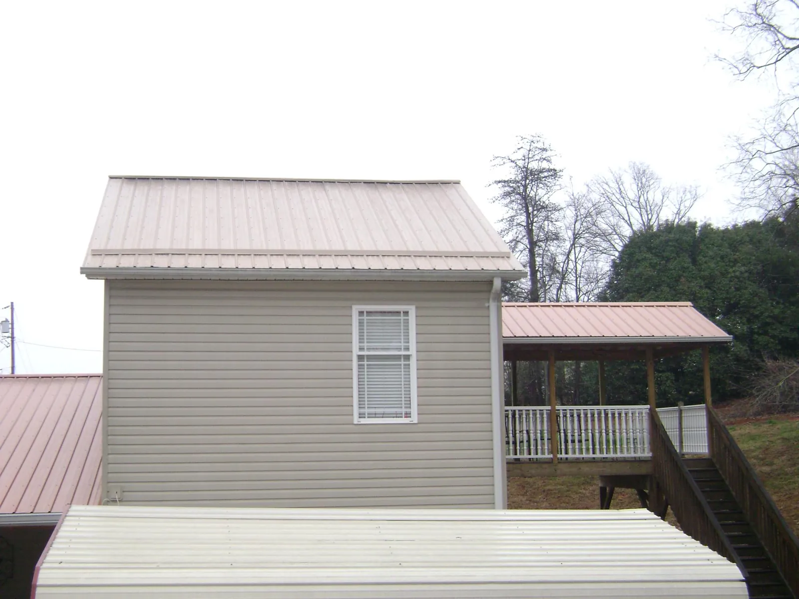 Tan metal roofs on a two story addition and attached porch, from a Roof Replacement job in Byron Center